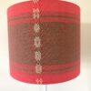 Colourful red lampshades handmade from South East Asian cotton in a drum shape.