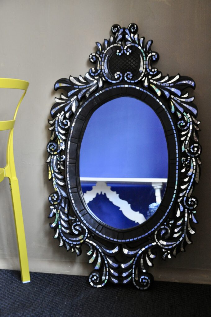 A charming, oval mirror from Thailand with intricate wood carving and mirrored glass decoration.