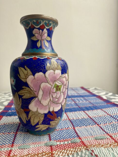 A colourful cloisonné metal vase with mauve pink floral décor against a cobalt blue backdrop.