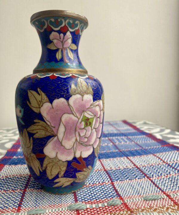 A colourful cloisonné metal vase with mauve pink floral décor against a cobalt blue backdrop.