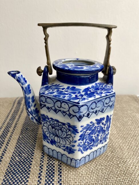 A decorative blue and white hand-painted Thai pottery teapot with lid and metal handle.