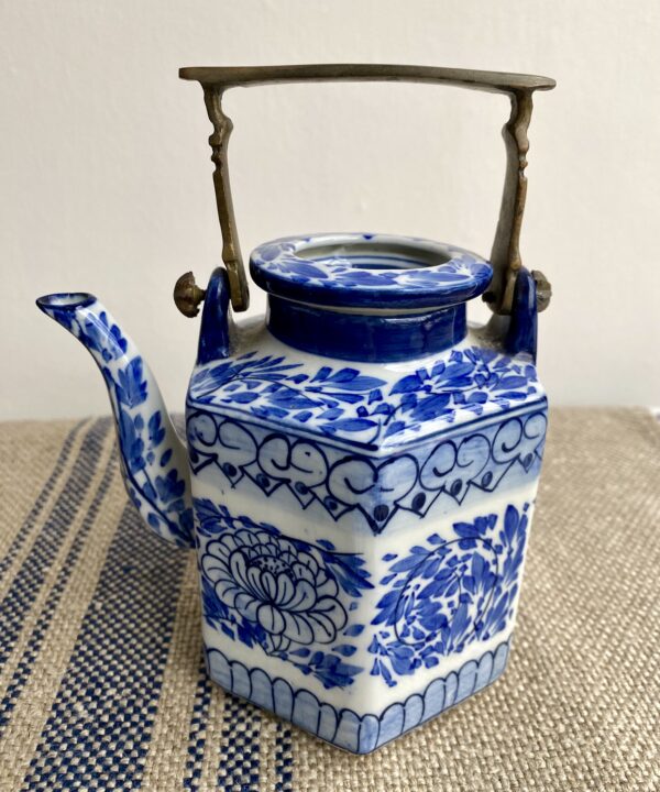 A decorative blue and white hand-painted Thai pottery teapot with lid and metal handle.