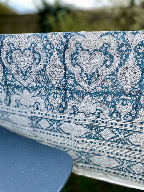 A slate blue patterned tablecloth in a garden setting with a modern blue chair.