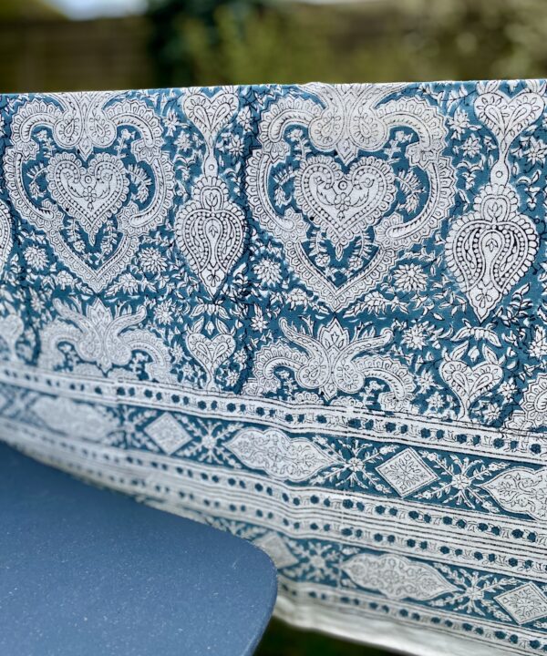 A slate blue patterned tablecloth in a garden setting with a modern blue chair.