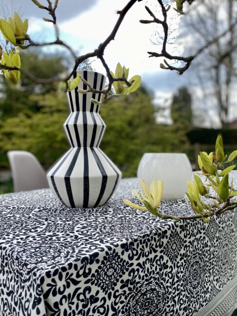 A monochrome tablescape with a stripy vase and magnolias in the foreground.