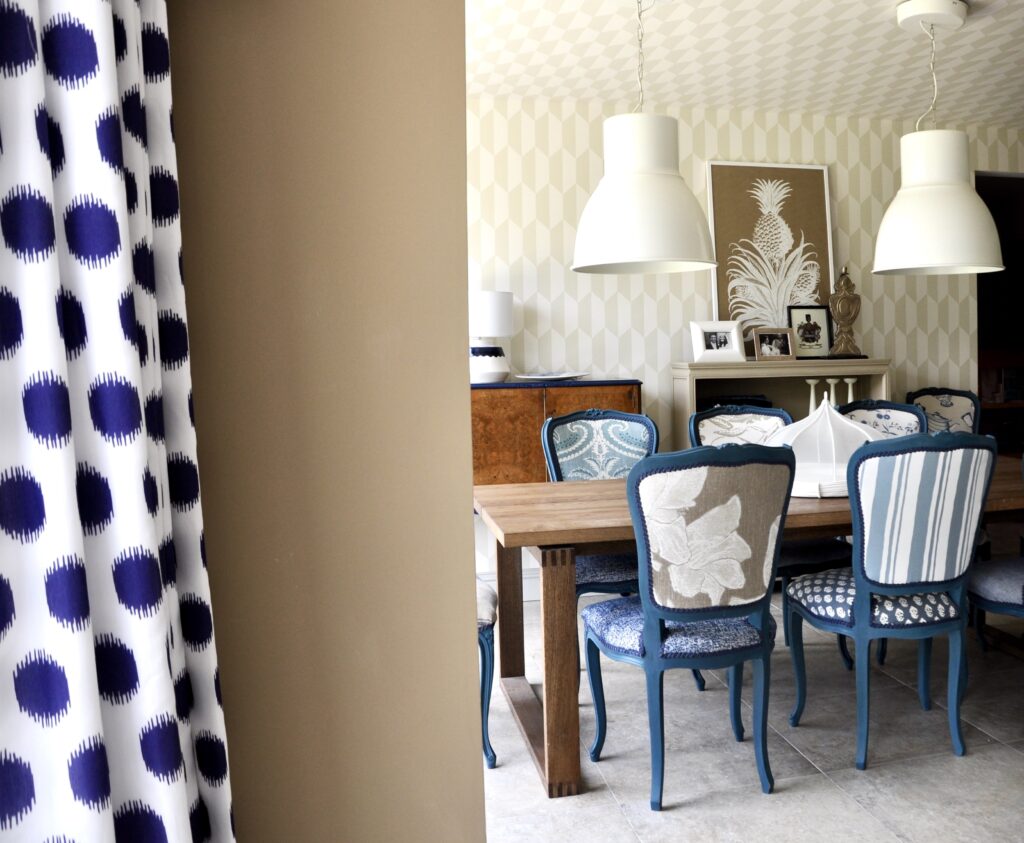 An elegant dining room in a blue, beige and cream scheme with large white pendant downlighters and blue-framed French-style dining chairs.