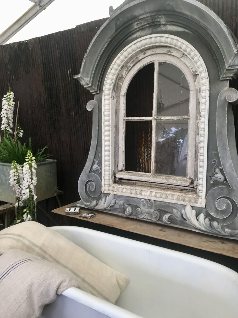 Architectural salvage in the form of an arched, French window in grey and white and decorated with scrolls and acanthus leaves.