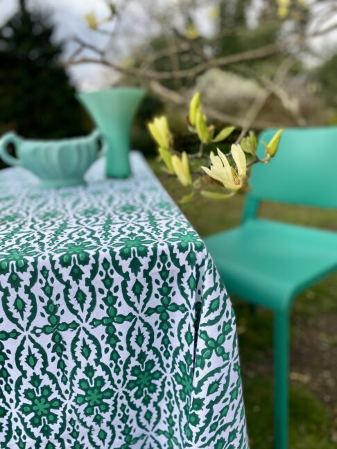 An outdoor table dressed with a bold, block print tablecloth with a modern green dining chair and sculptural, green vases.