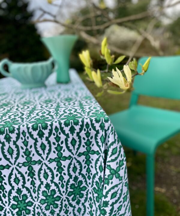 An outdoor table dressed with a bold, block print tablecloth with a modern green dining chair and sculptural, green vases.