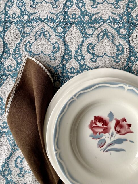 Vintage floral French dishes with brown linen napkin on a blue patterned tablecloth.