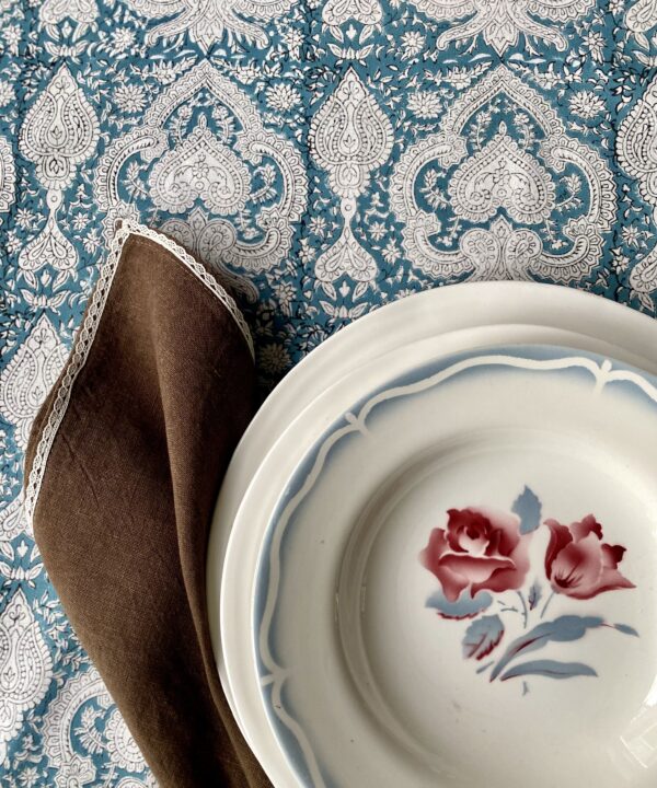 Vintage floral French dishes with brown linen napkin on a blue patterned tablecloth.