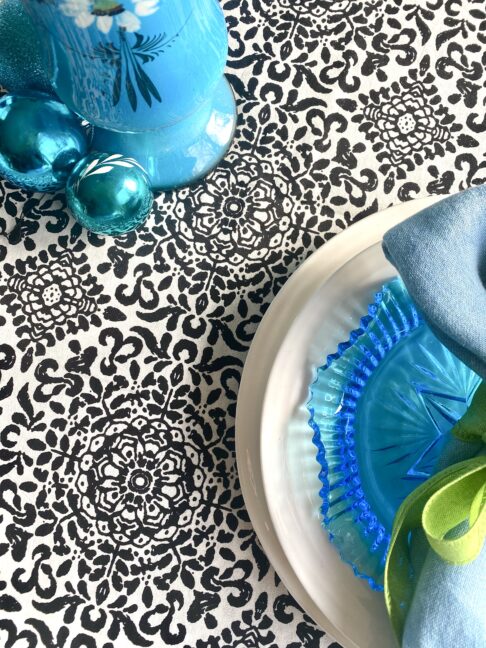 Detail of a black and white patterned tablecloth with turquoise tableware and decorations.