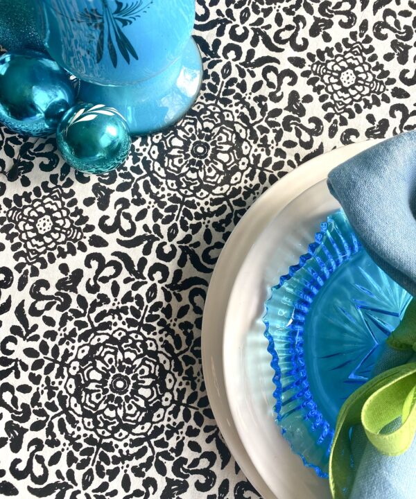 Detail of a black and white patterned tablecloth with turquoise tableware and decorations.