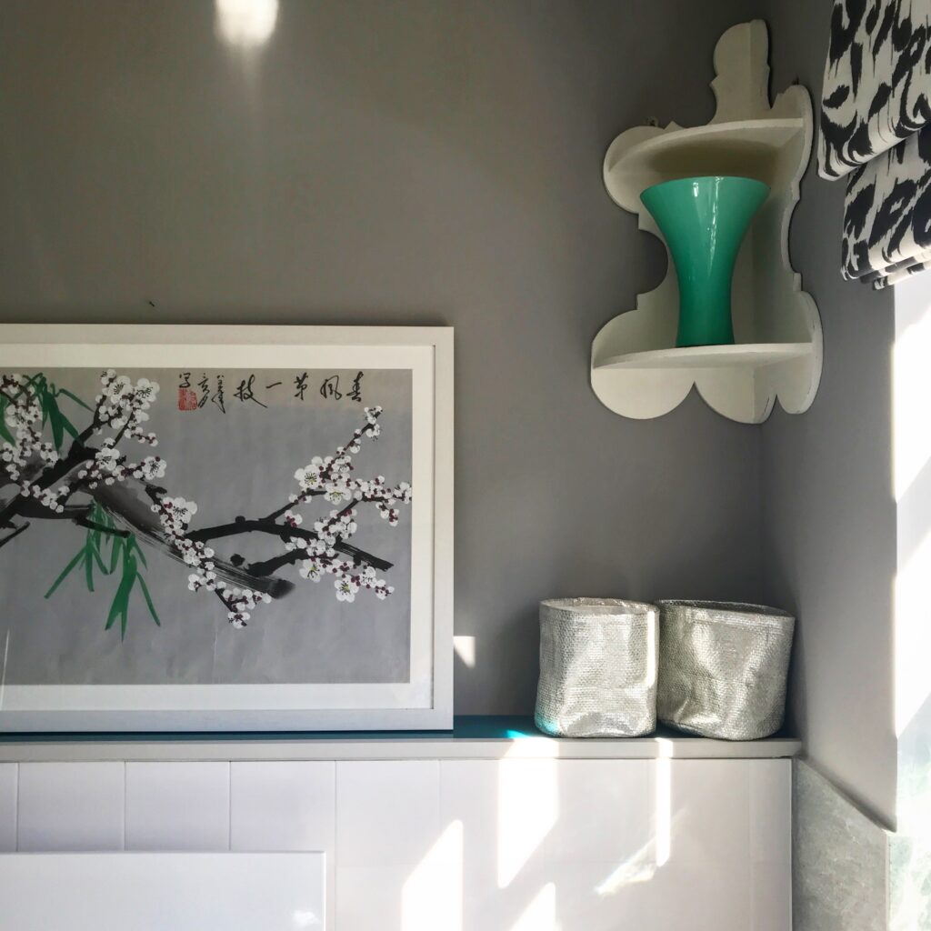 A pretty bathroom wall with a curvy, corner shelf and a framed, Asian blossom painting in greys and jade green hues.