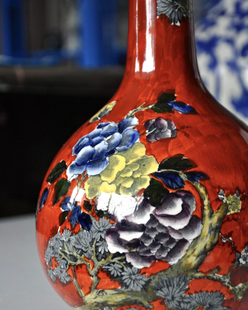 Detail of a striking, Asian-style bottle vase in rust red with floral decoration in blue, yellow and mauve.