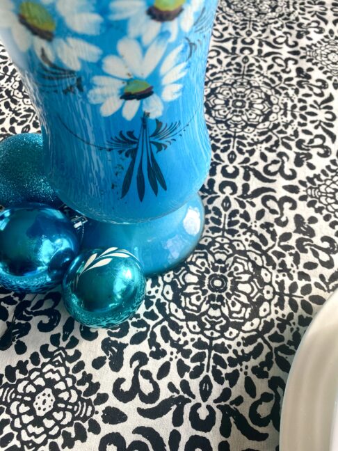 Detail of a monochrome black and white tablecloth with turquoise vase and baubles.