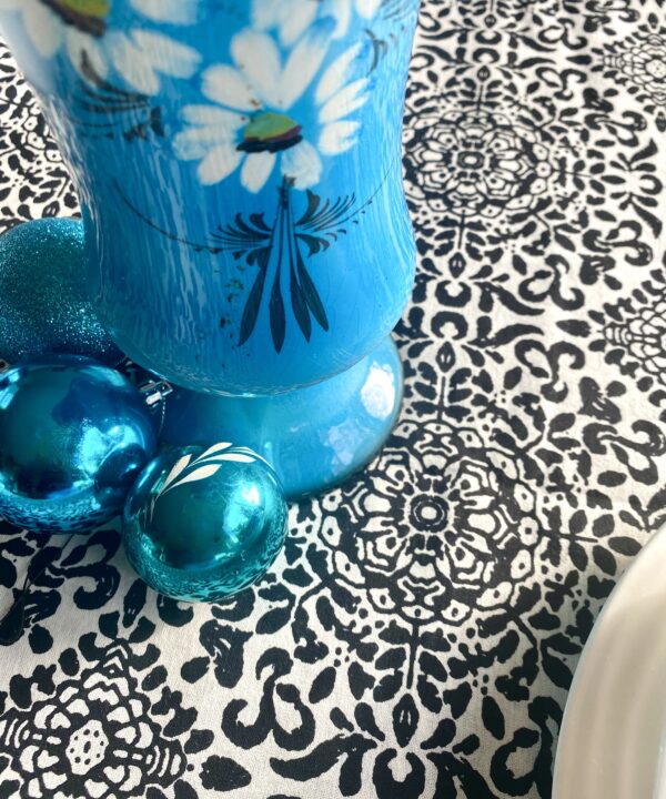 Detail of a monochrome black and white tablecloth with turquoise vase and baubles.