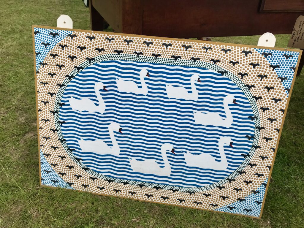 A painted, decorative board in blue and white depicting a bevy of swans on a river.