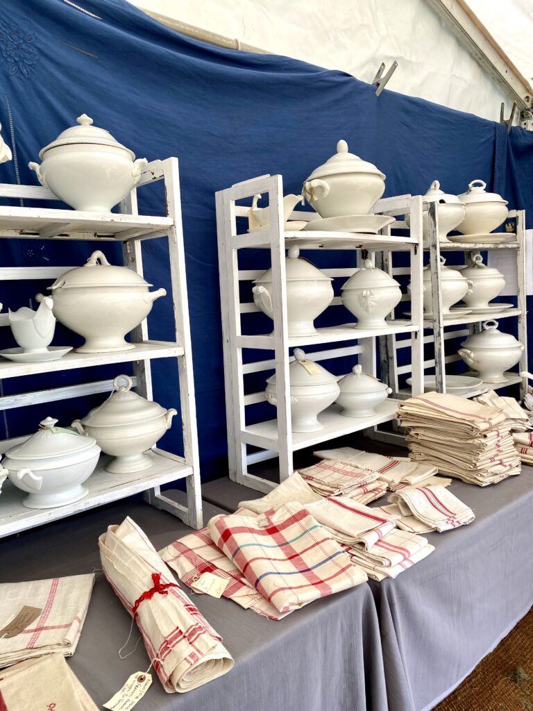 Shelves of vintage, French tureens in white alongside red check table linen.