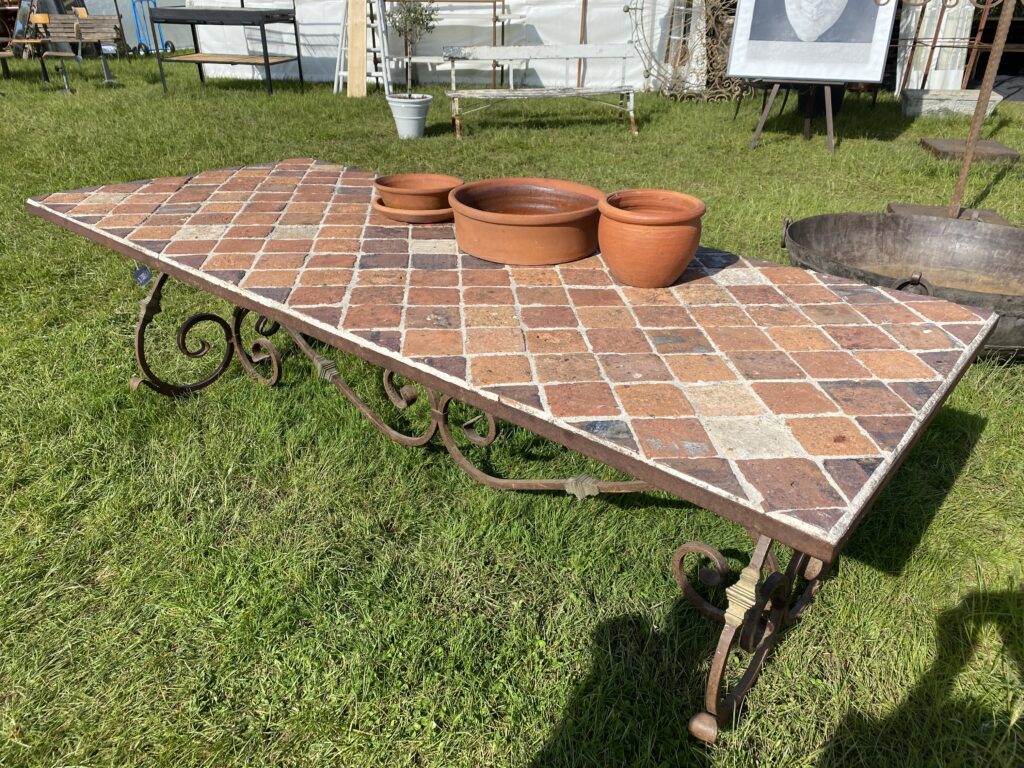 A terracotta-tiled, Italianate outdoor table with a wrought iron base.