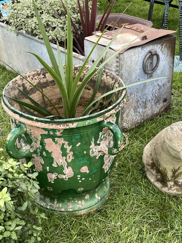 A large, distressed, vintage, urn-shaped, garden planter in green with handles.