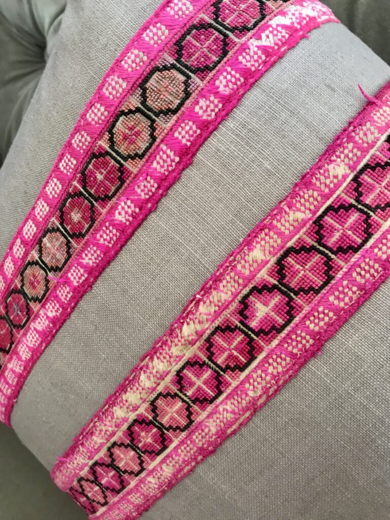 A beige glazed linen cushion with two decorative trims of vintage, Thai, embroidered textiles in bright pink.