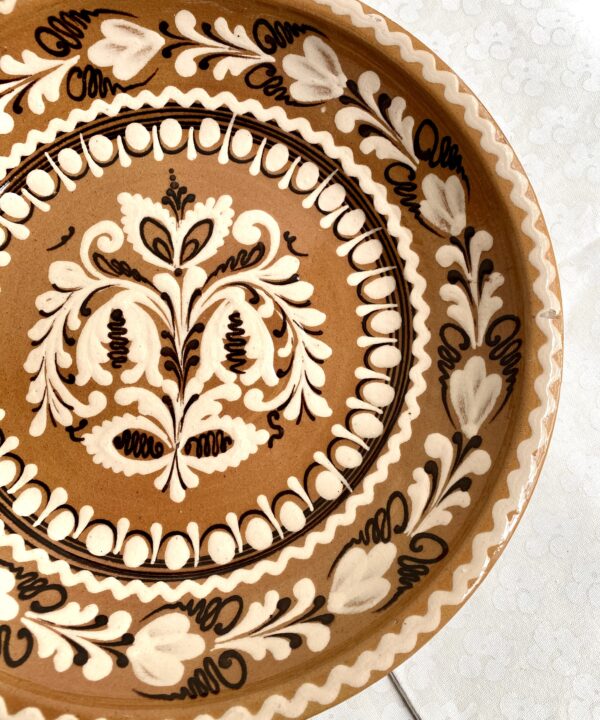 A rustic, Hungarian pottery plate for display in browns, creams and terracotta hues.