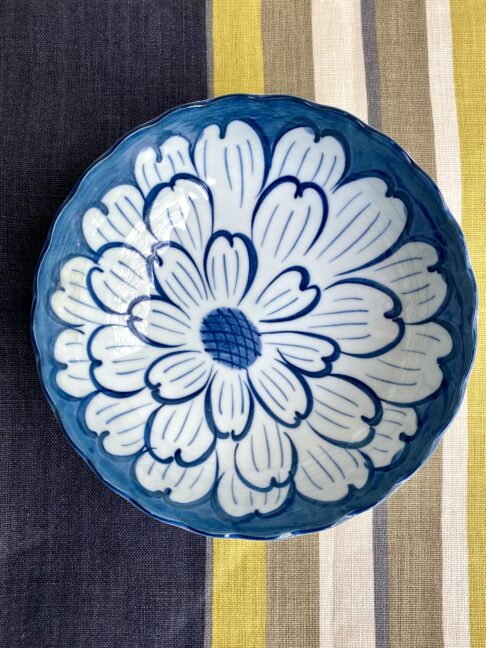 A vintage Japanese ceramic bowl with indigo flower decoration on a striped linen tablecloth in navy, taupe and chartreuse.