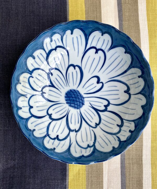 A vintage Japanese ceramic bowl with indigo flower decoration on a striped linen tablecloth in navy, taupe and chartreuse.