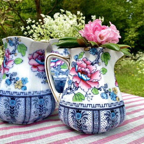 Antique floral jugs in a variety of sizes in an outdoor setting.