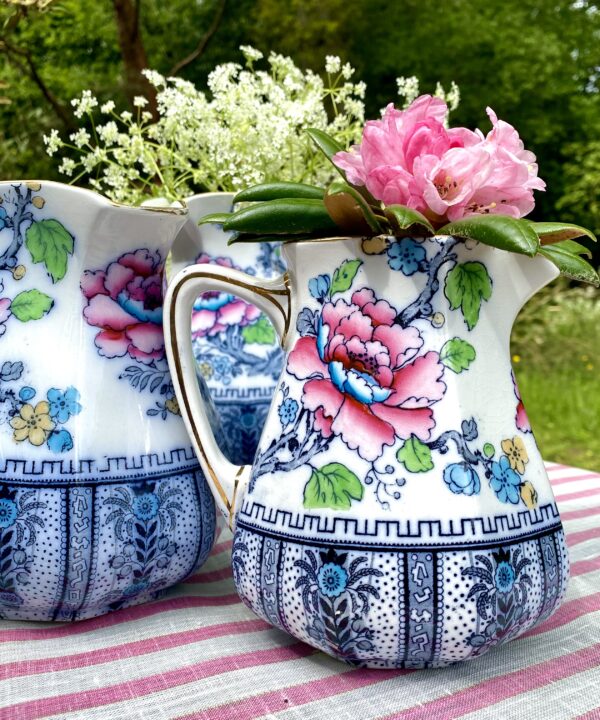 Antique floral jugs in a variety of sizes in an outdoor setting.