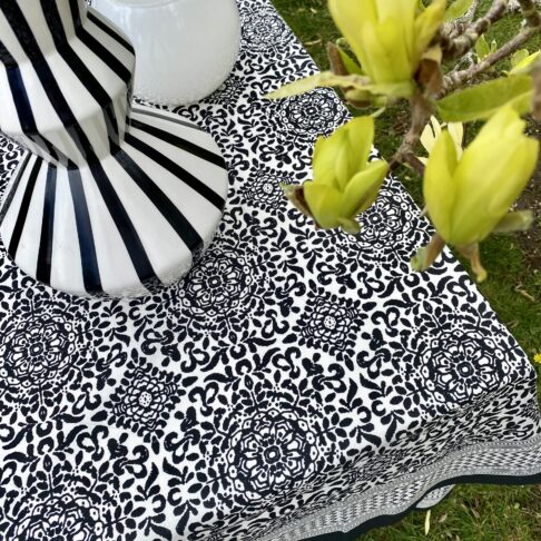 A black and white block-printed, Indian tablecloth in cotton with yellow magnolia in the foreground.