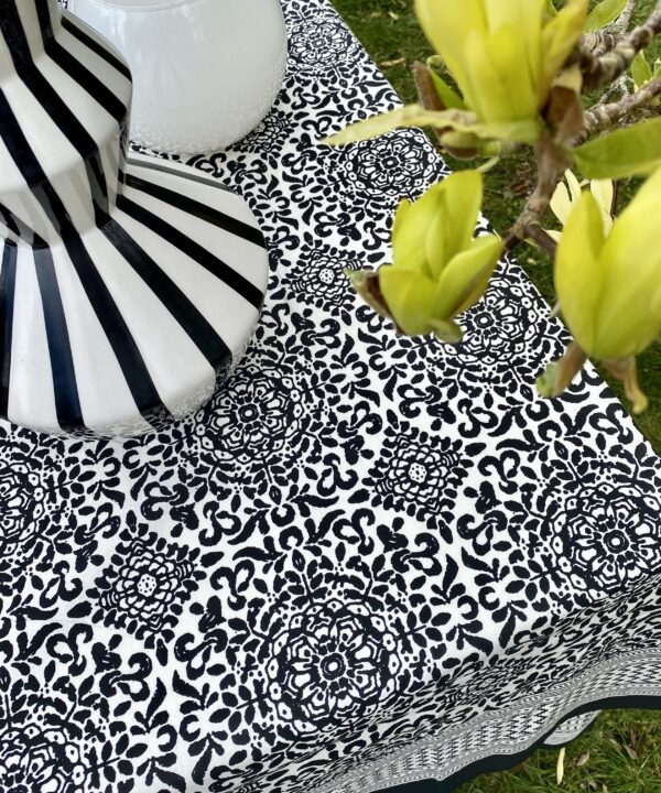 A black and white block-printed, Indian tablecloth in cotton with yellow magnolia in the foreground.