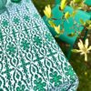 A green patterned tablecloth with an Indian block print design styled with green vases and a chair in an outdoor setting.