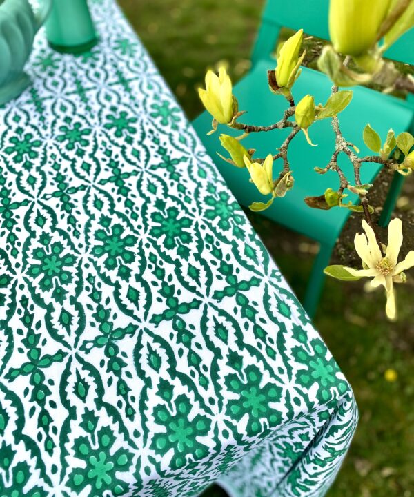 A green patterned tablecloth with an Indian block print design styled with green vases and a chair in an outdoor setting.