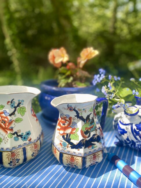 Pretty, vintage floral jugs with blue and orange decoration styled on an outdoor table.