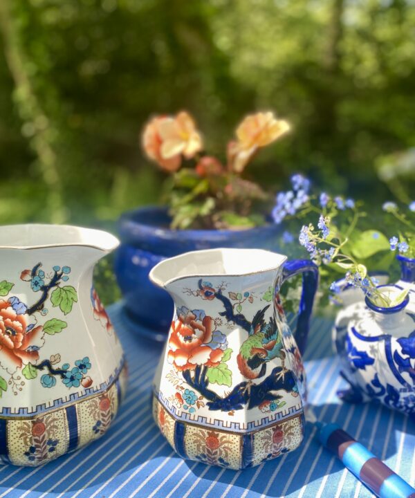 Pretty, vintage floral jugs with blue and orange decoration styled on an outdoor table.