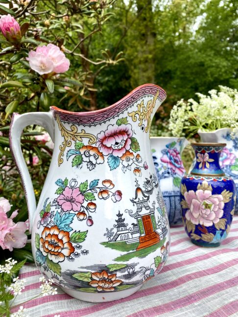 A vintage floral jug in pink and orange with Chinese-inspired motifs in an outdoor setting.