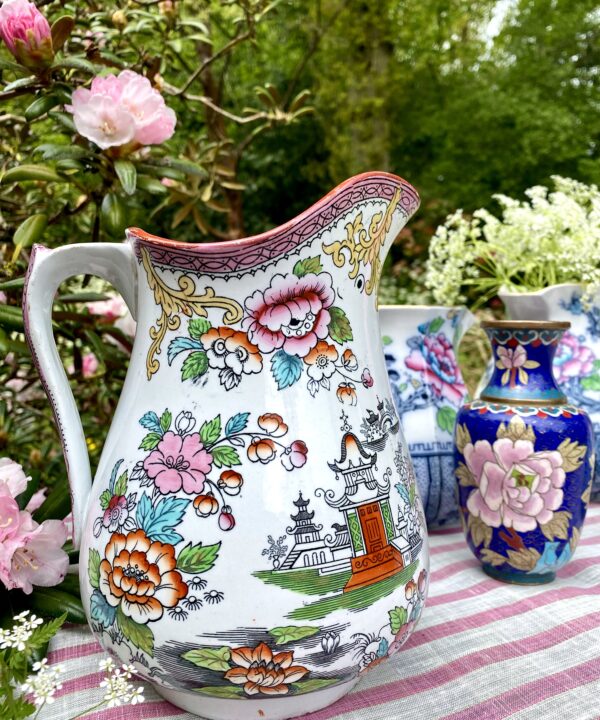 A vintage floral jug in pink and orange with Chinese-inspired motifs in an outdoor setting.