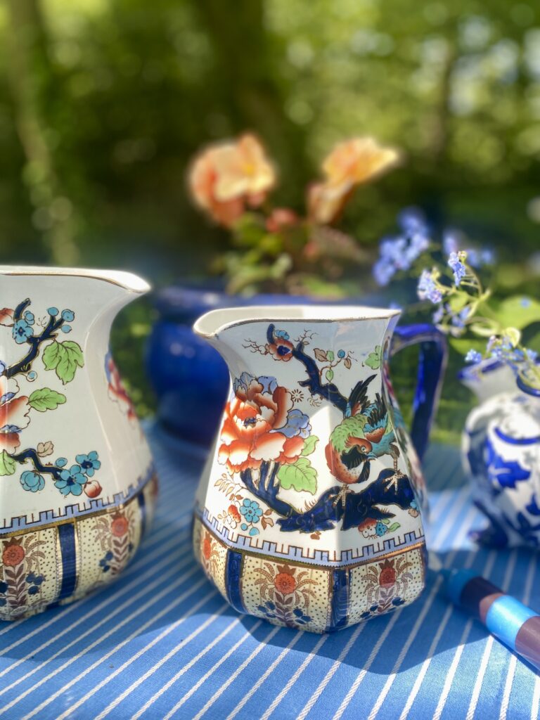 Blue and orange vintage china jugs on a blue striped tablecloth in the summer sunshine.