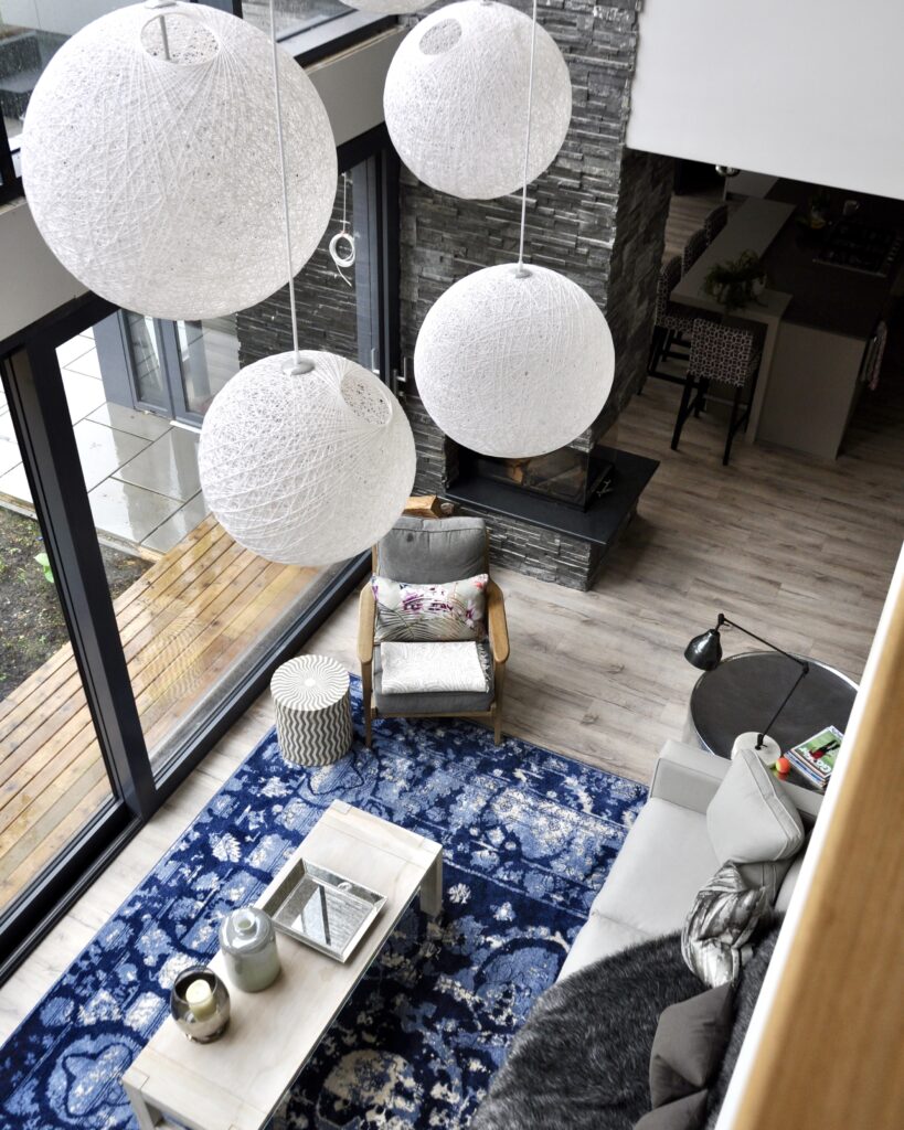 An overhead shot of a contemporary sitting room with a grouping of white ball pendants lights and an over-dyed blue and white Turkish rug.