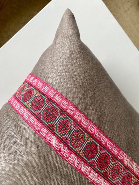 A vintage, pink embroidery trim on a taupe cushion.