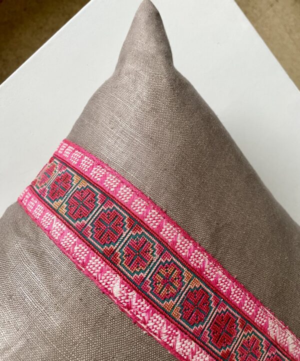 A vintage, pink embroidery trim on a taupe cushion.