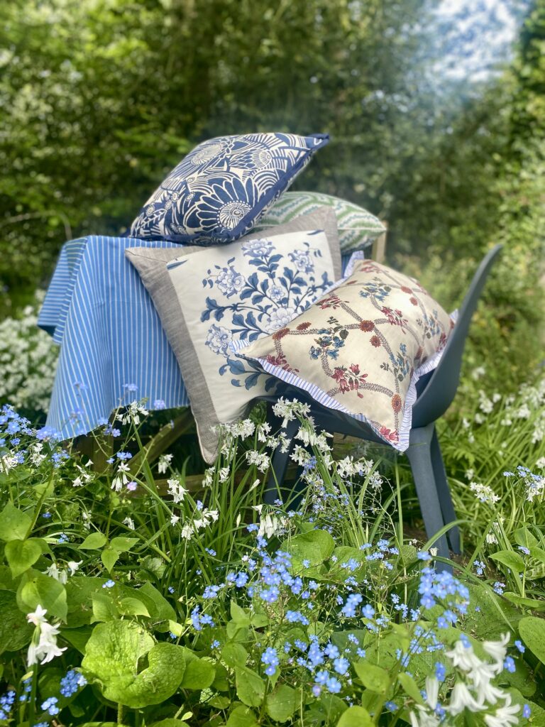 A pile of blue, green and pink floral cushions on a chair in a Spring garden setting.