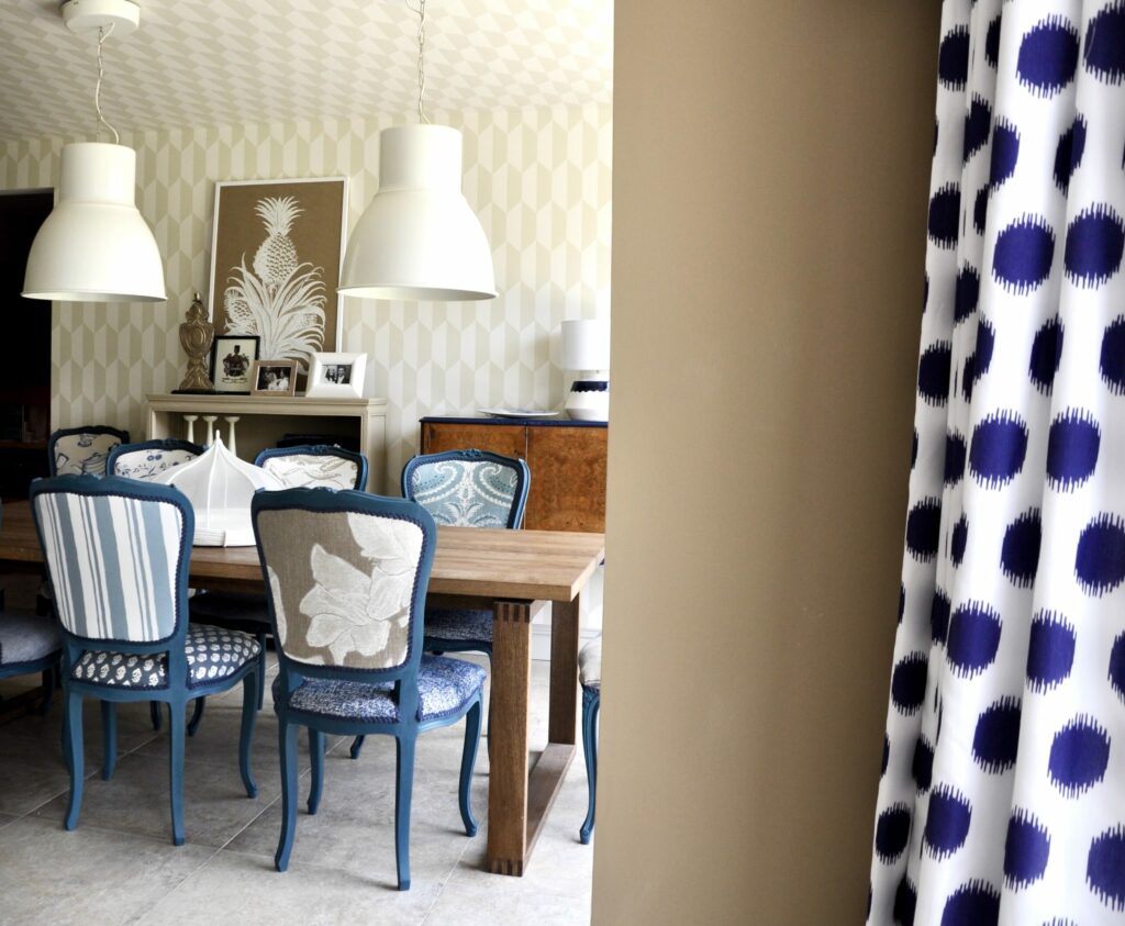 A beige and blue dining room scheme featuring painted French dining chairs in blue and an Ikea polka dot print curtain in the foreground.