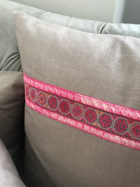 A taupe linen cushion with pink embroidered trim.