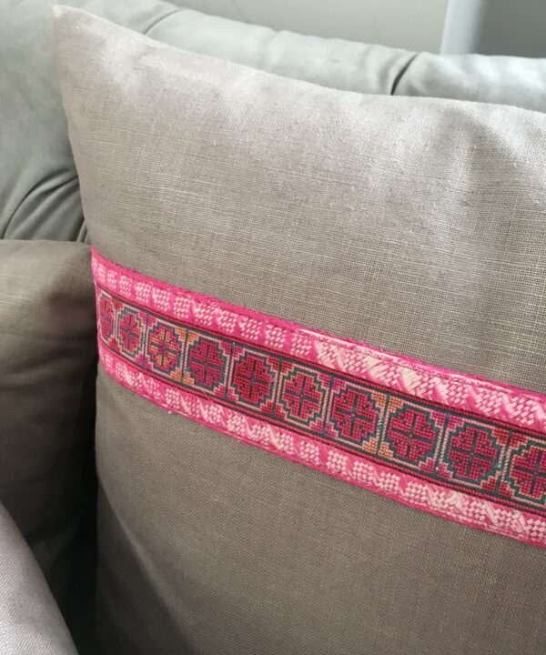 A taupe linen cushion with pink embroidered trim.