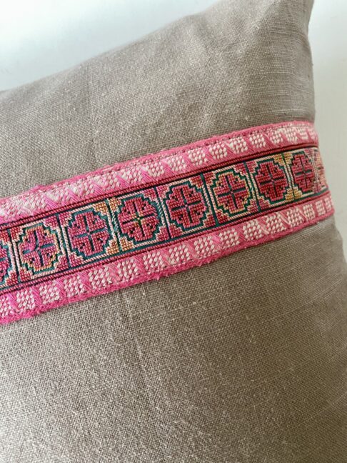 Detail of a pink embroidered braid trim on a linen cushion.