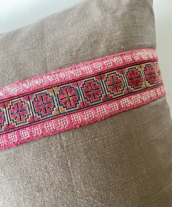 Detail of a pink embroidered braid trim on a linen cushion.