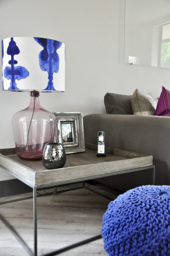 A neutral sitting room coffee table featuring a pink glass table lamp with a striking blue drum shade in a print by fabric house Korla.